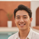 Smiling young adult of East Asian descent, with a joyful and relaxed expression, against a blurred background with warm amber